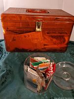 Amber plastic sewing box with closed lid and round container with sewing packets in front.