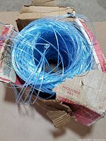 Top view showing blue coiled twine inside torn cardboard box with visible warnings and instructions.