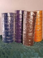 Stack of several rolls of electrical tape in blue, purple, brown, and orange colors wrapped in plastic