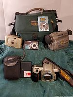 Photo of all camera equipment and accessories laid out in front of Tamrac camera bag on green fabric background.