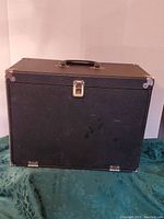 Closed view of the vintage black make-up travel box with handle and metal corner protectors.