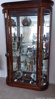 Full front view of the wood curio cabinet showing curved glass front, three glass shelves, and various collectible items on display.
