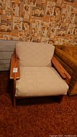 Front view of the wooden frame lounge chair with beige cushions, showing the chair's structure and fabric texture.