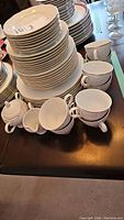 Full view of stacked plates and some cups arranged with creamer and sugar bowl on table.