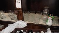 Photo showing assorted old fashioned glasses with diamond cut glass pattern, plain glasses, glass snowman jar, and salt and pepper shakers