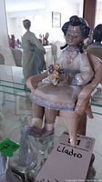 Front view of Lladro porcelain figurine depicting a young girl with bows in her hair sitting in a pink chair holding a bouquet of flowers.