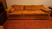 Front view of three-seat sofa showing orange textured upholstery and two cylindrical bolster pillows