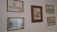 Five framed prints mounted on wall showing detailed black and white architectural and urban scenes