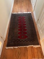 Full length view of the machine woven rug on hardwood floor showing its geometric pattern and fringe.