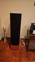 Front view of one floorstanding speaker showing black fabric grille and cherry wood veneer base