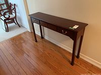 Front and angled view of dark wooden console table with three drawers along a wall, showing left and right drawers with handles, middle drawer without handle.