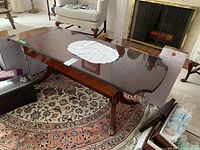 Angle view of polished dark wood coffee table showing smooth top surface, curved edges, and metal claw guards on feet.