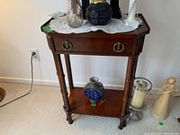 Front view of the wood side table showing top surface with items, one drawer with ring pull handles, and lower shelf.