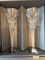 Pair of Waterford crystal champagne flutes shown together inside original packaging box showcasing the cut crystal design and long stems.
