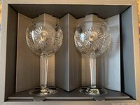 Pair of Waterford crystal goblets inside original packaging, showing starburst cut pattern on the bowl and long faceted stems.