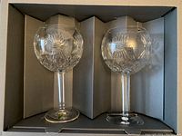 Two Waterford crystal goblets arranged side by side inside a gray box with compartments, showing full front view, clear crystal with cut starburst patterns.