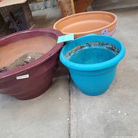 Overview of three plant pots: maroon/brown, terra cotta, and blue pots placed on concrete floor.