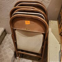 Six stacked Samsonite padded folding chairs with beige frames and fabric padding.