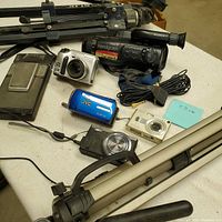 Wide shot of five cameras and two tripods on a table.