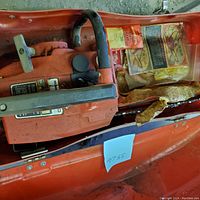 Top view of orange Homelite Textro gas chainsaw inside the orange carrying case with visible components and part of the manual/instructions.