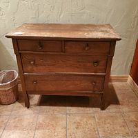 Front view of a small pine wood chest of drawers with four drawers, showing surface wear and wooden knobs on each drawer.