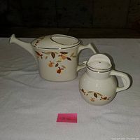 Flower pot and syrup pitcher shown together on a white cloth background, showing decorative Autumn Leaf pattern.