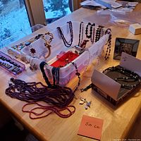 Wide view of various costume jewelry items including beaded necklaces and bracelets spread out on a table with a clear plastic container