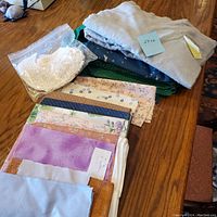 Assorted folded cotton fabrics, including flannel, with various colors and patterns, and a bag of white lace pieces