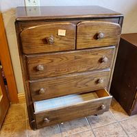 Front view of wooden four drawer dresser with drawers partially open, showing wood grain finish and knob handles.
