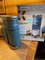 Photo of the Keurig K-Mini Plus single cup coffee maker with its box in the background on a wooden surface.