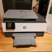 Front view of HP OfficeJet Pro 8034e printer with paper output tray open, touchscreen lit, device powered on.