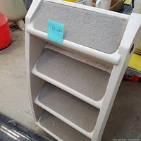 Oblique view of pet steps showing four gray carpeted steps on off-white plastic frame with side rails.