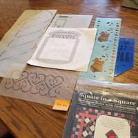 Photo of various quilting templates and stencils made of clear plastic, with designs including leaves, hearts, and a teddy bear stencil with leaves and feathers, along with printed instructions.