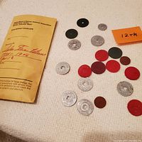 Collection of aluminum and plastic Colorado sales tax tokens from 1934 to 1946 alongside a coin deposit envelope.