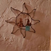 Metal starburst wall decor with two copper-colored coyote figures inside circular center, mounted on textured wall.