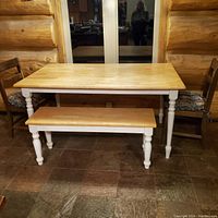 Full view of the hardwood rectangular dining table with white legs, two wooden chairs with floral cushions, and wooden bench.