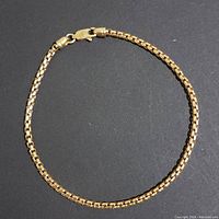 Full view of 14k yellow gold box-link bracelet laid flat on black background.