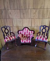 Set of three miniature chairs, two wooden with armrests and one loveseat-style, upholstered in red striped fabric with decorative motifs.