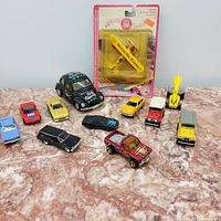 Various diecast cars including a yellow airplane model in original packaging and colorful Volkswagen Beetle model on marble background