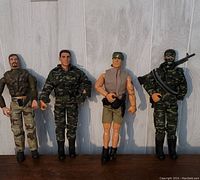 Four vintage military action figures standing upright against a light wood panel background, showing details of clothing, gear and weaponry.