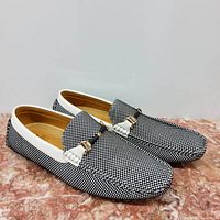 Side angle of men's black and white patterned loafers with white trim and metallic buckle detail.