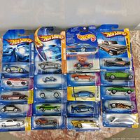 Top view of 20 Hot Wheels die-cast cars in original blister pack packaging arranged in 4 columns and 5 rows, showing various designs and colors with Hot Wheels branding on packaging.