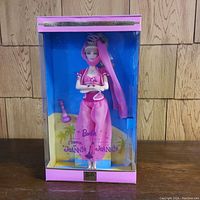 Front view of Barbie doll in original sealed box showing doll in pink genie costume with clear box front and pink/blue themed packaging.