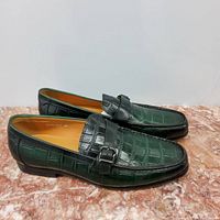 Side view of men's leather loafers with crocodile embossing and black buckle detail on a marble surface.