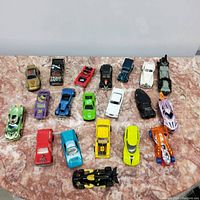 Top-down photo showing 20 assorted small toy collector's cars in multiple colors and styles arranged in four rows on a flat surface.