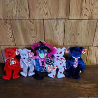 Five Beanie Babies displayed side by side on a wooden surface against wood paneling. Each has its Ty signature heart tag visible, showing a variety of characters and themes.