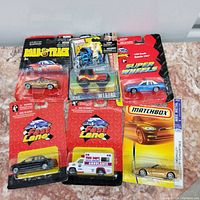 Photo showing six collector's cars in original packaging from various brands such as Super Wheels, Marvel, Road Track, Matchbox, and Fast Lane.