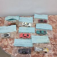 Photo showing 8 individually bagged collector cars with handwritten note labels laying on a marble surface.