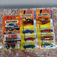 Eight Matchbox die-cast vehicles in original blister card packaging of various models and colors. Visible model names include Snow Groomer, Dirt X, Chevy Stepside, Shelby GT500, and more.