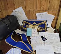 Overall view of Masonic regalia aprons, documents, and carrying case spread out on wooden surface